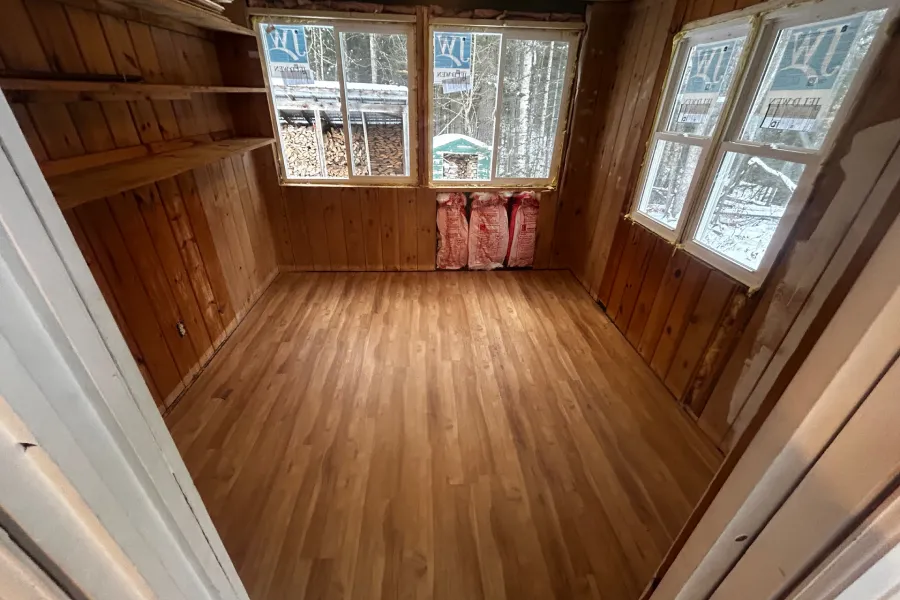 An empty wooden room with shelves on the left wall, three new windows, and rolls of insulation underneath.